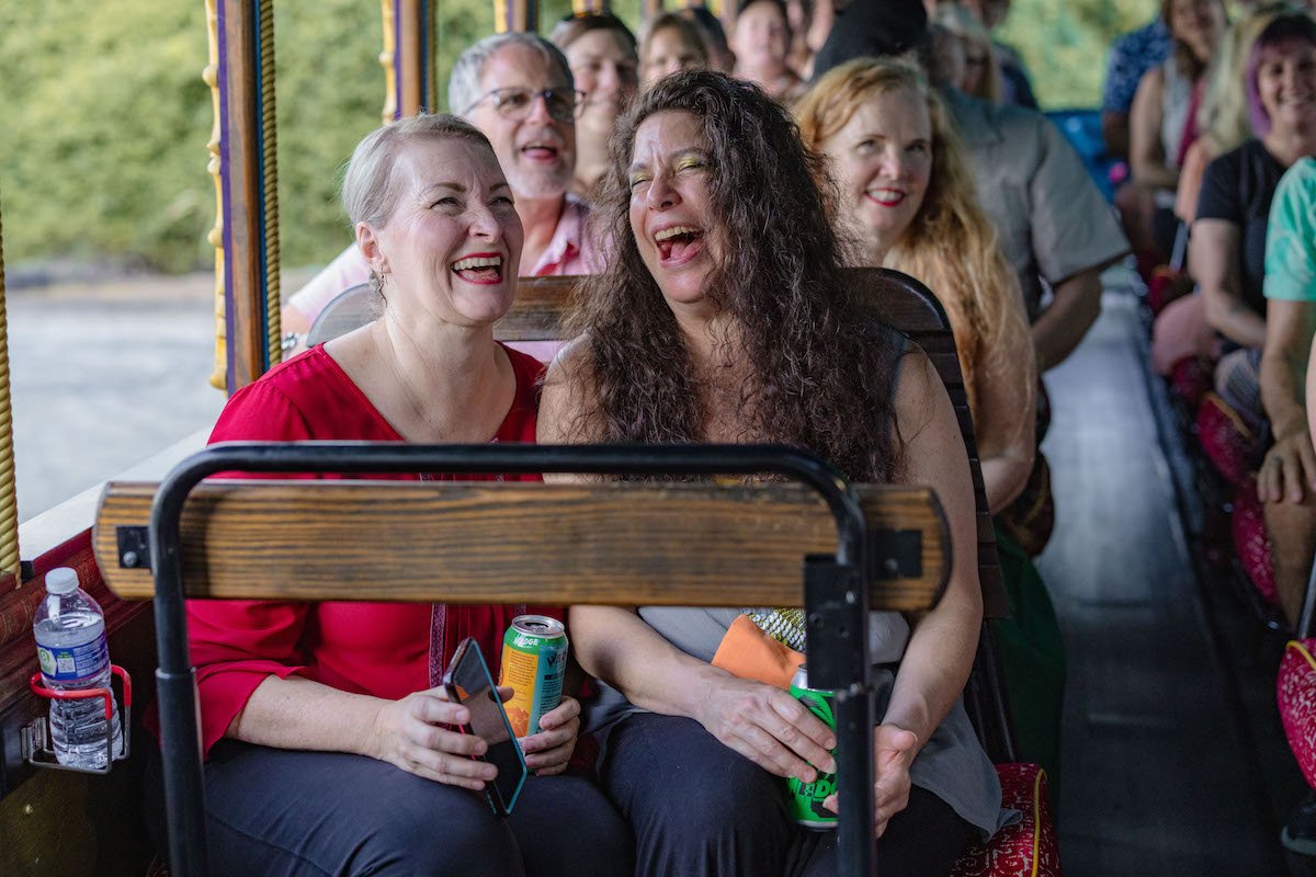 Close up of two women on the bus, enjoying a laugh and a beer.