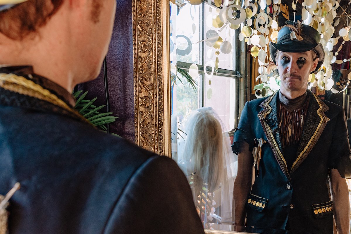 Bones, An Undead Tour Guide, looks at himself in a victorian gold framed mirror